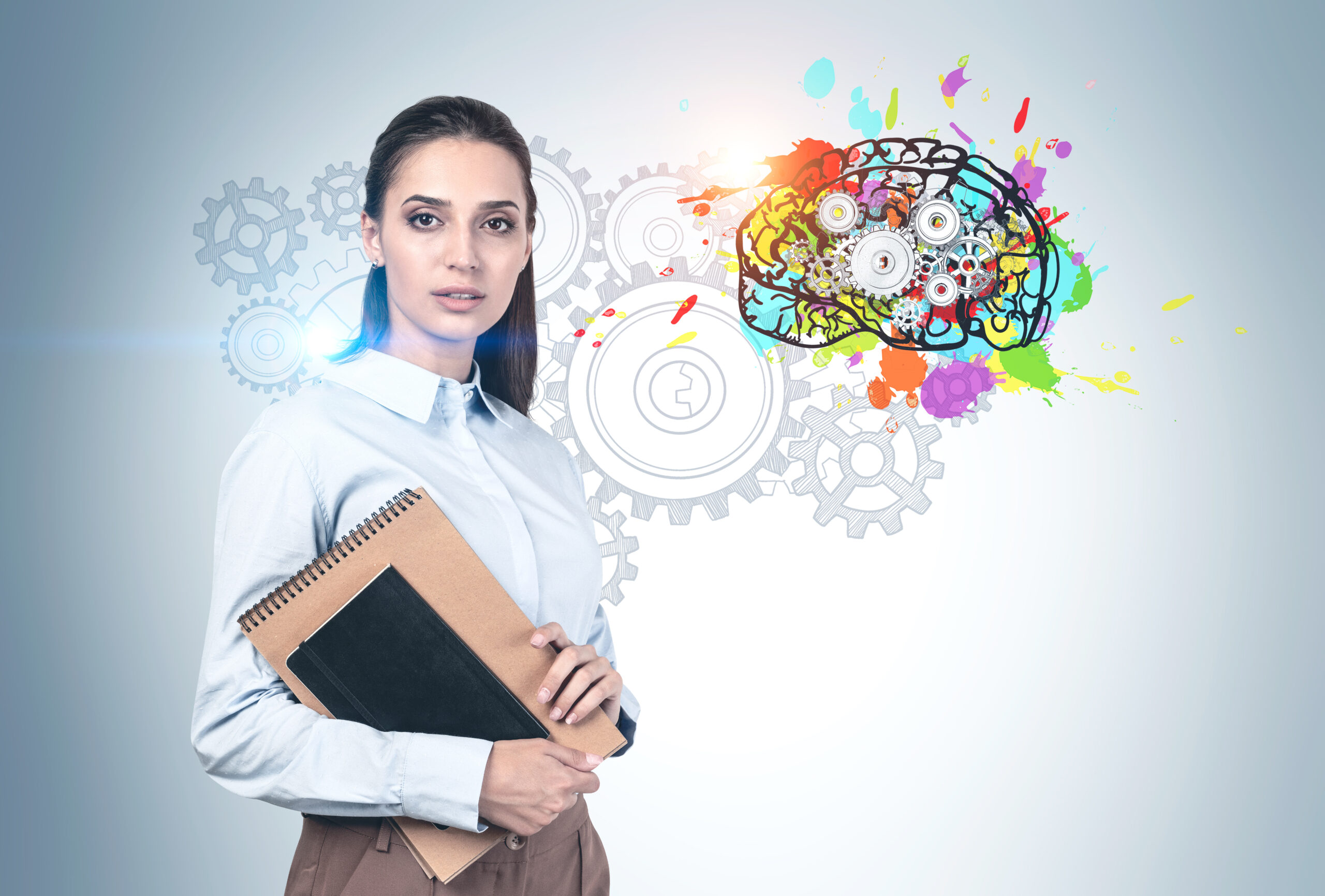 Serious young woman with dark hair and notebooks standing near concrete wall with colorful brain with gears drawn on it. Concept of brainstorming and education.